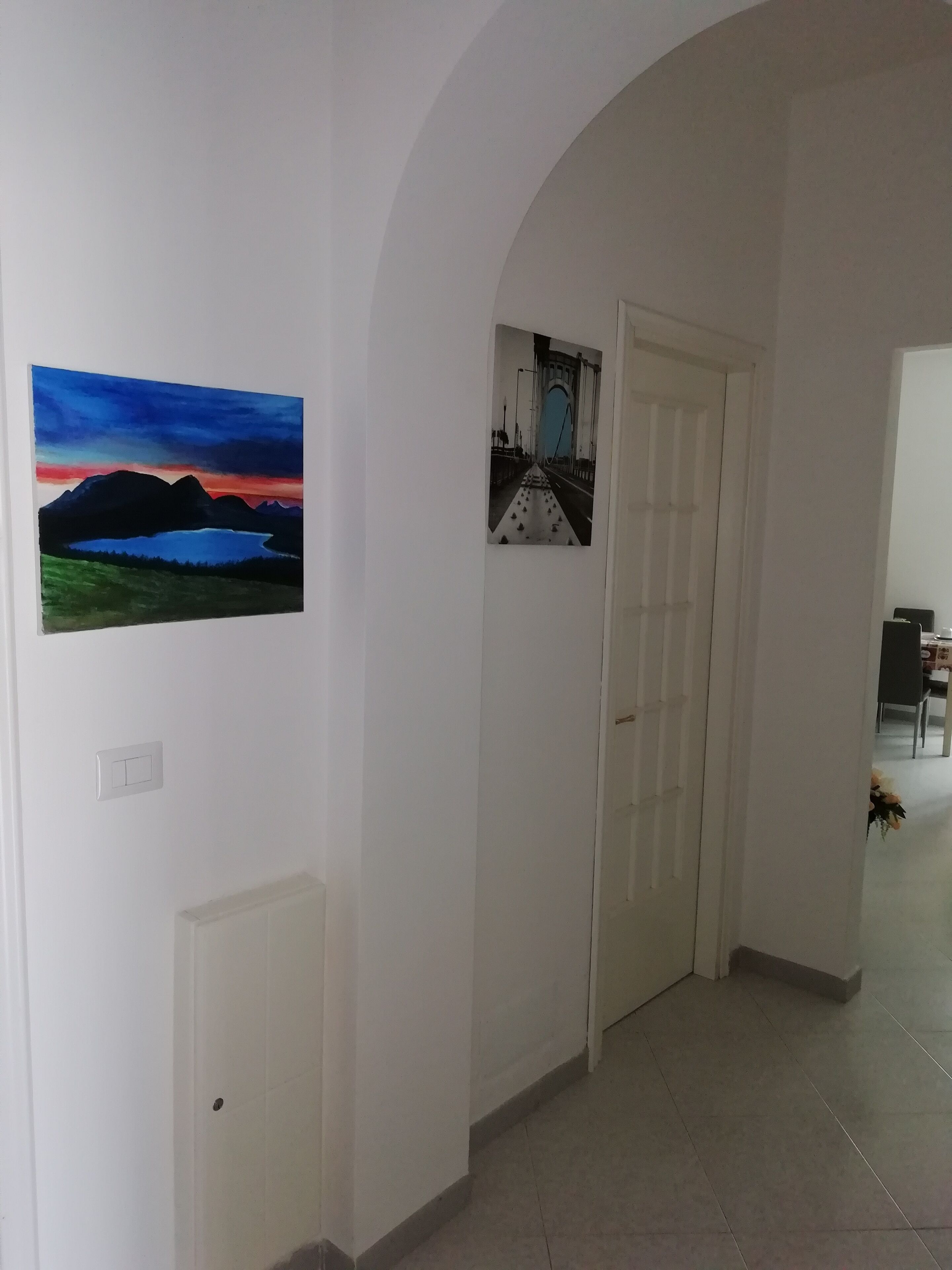 A hallway with two doors, a painting of a landscape, and a framed photo of a bridge.