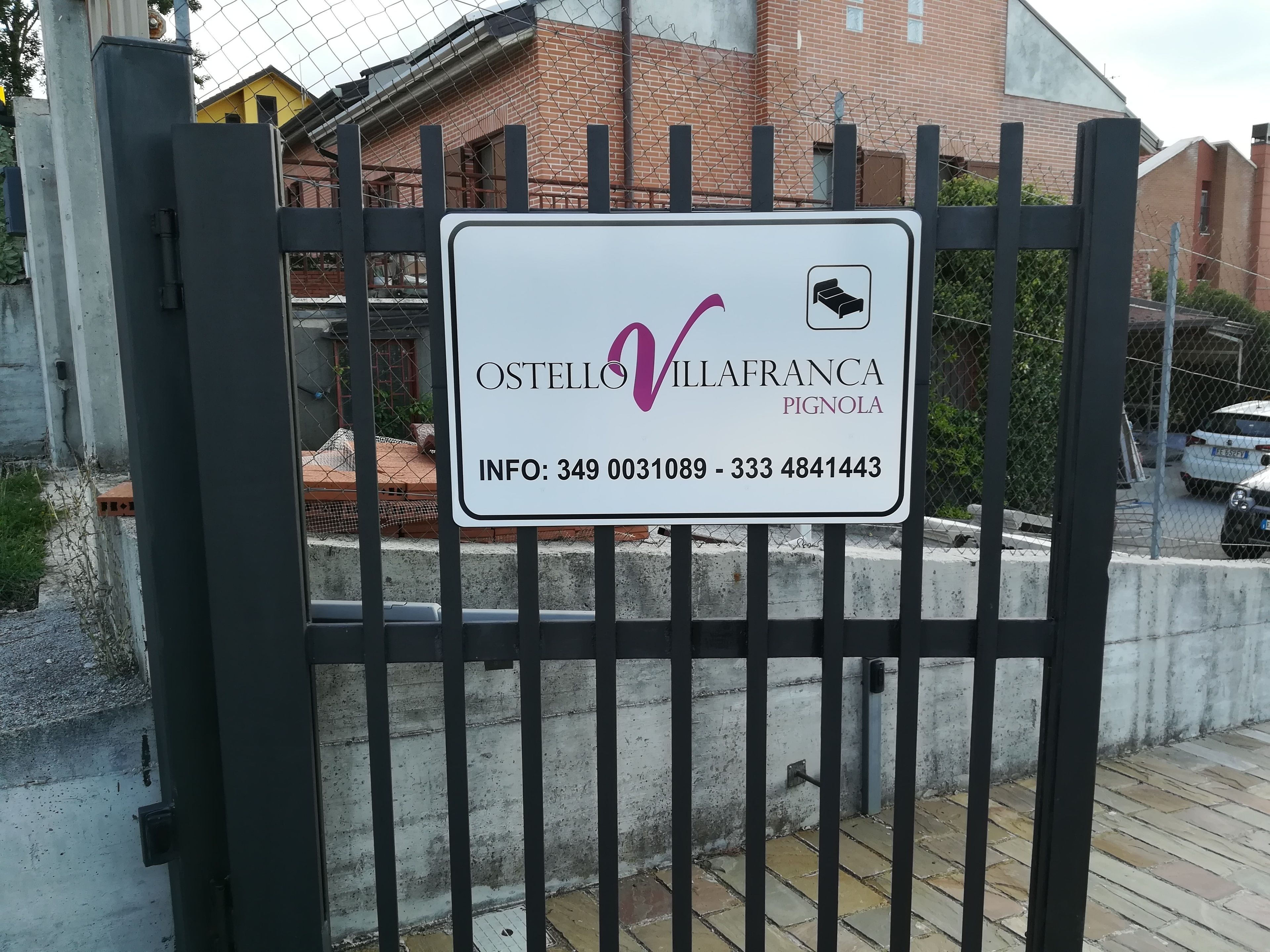 A gated entrance with a sign for Ostellovilla Franca Pignola, including contact information.
