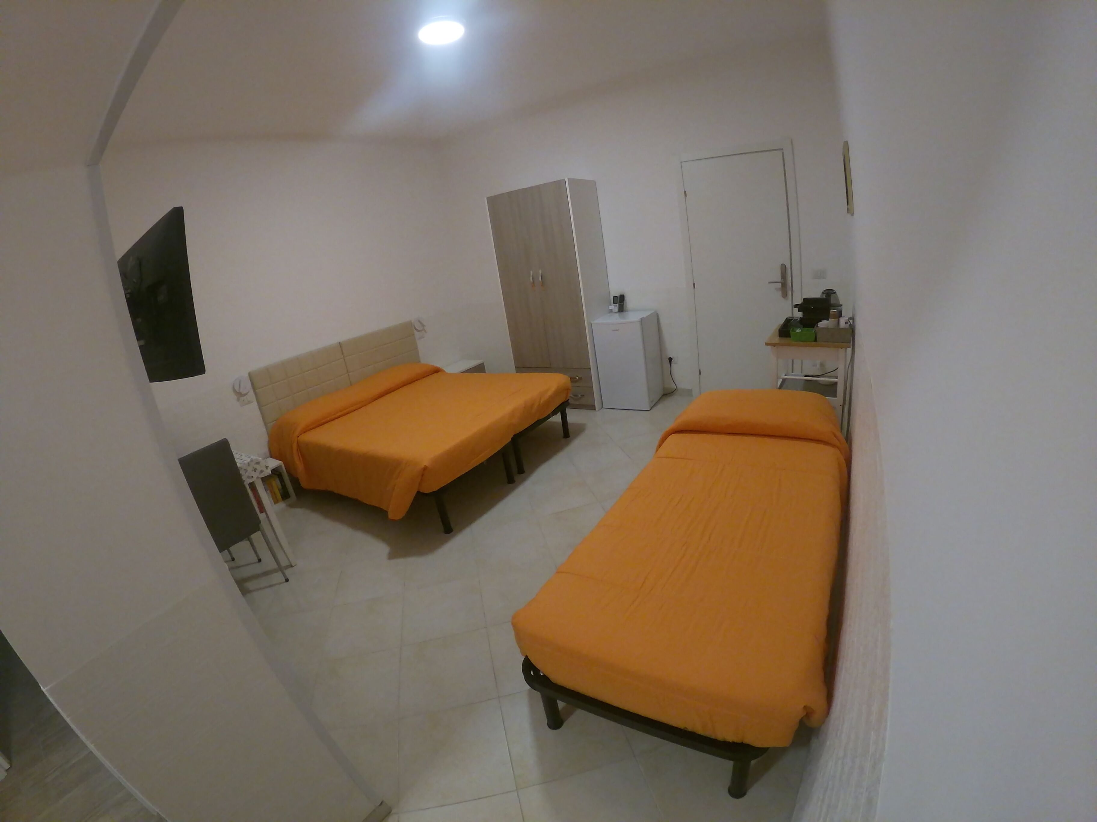 A room with two single beds, a small desk with a chair, a wardrobe, and a cabinet.