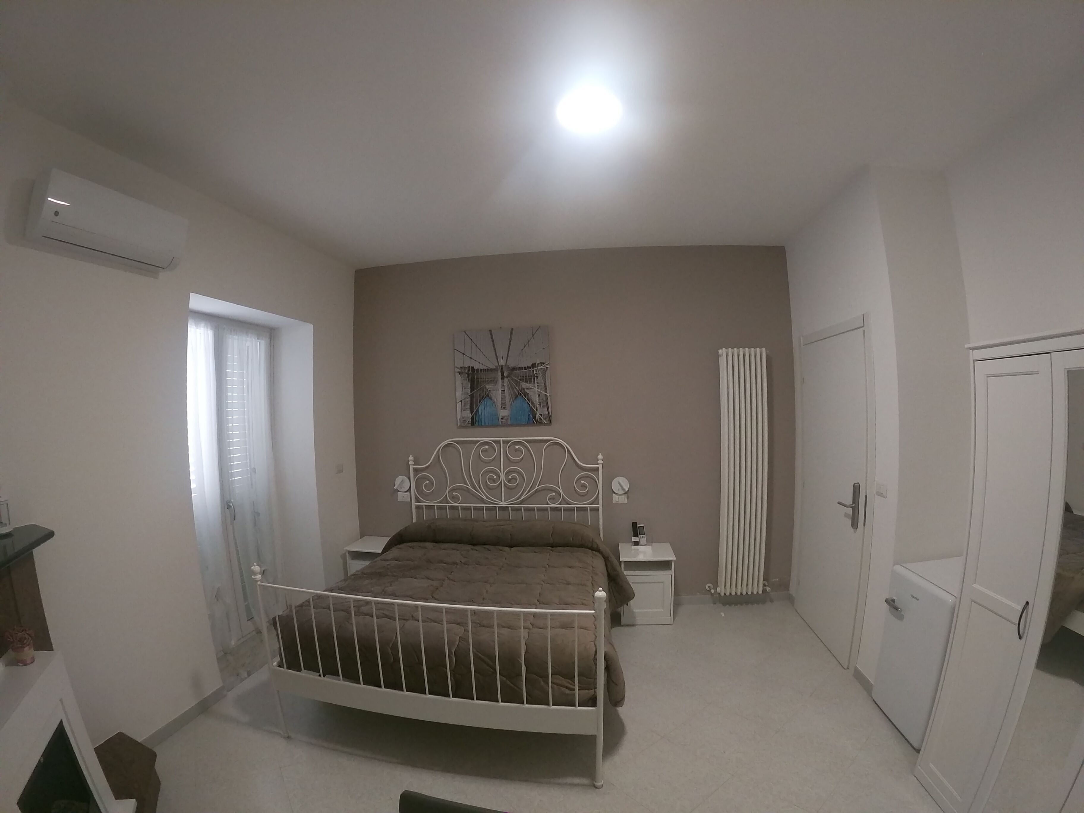 Un dormitorio con cama, mesitas de noche, un radiador, un armario y un equipo de aire acondicionado.