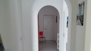 A hallway with a white door at the end, a red chair, and a bookshelf with books. - Ostello Villafranca (Pignola)