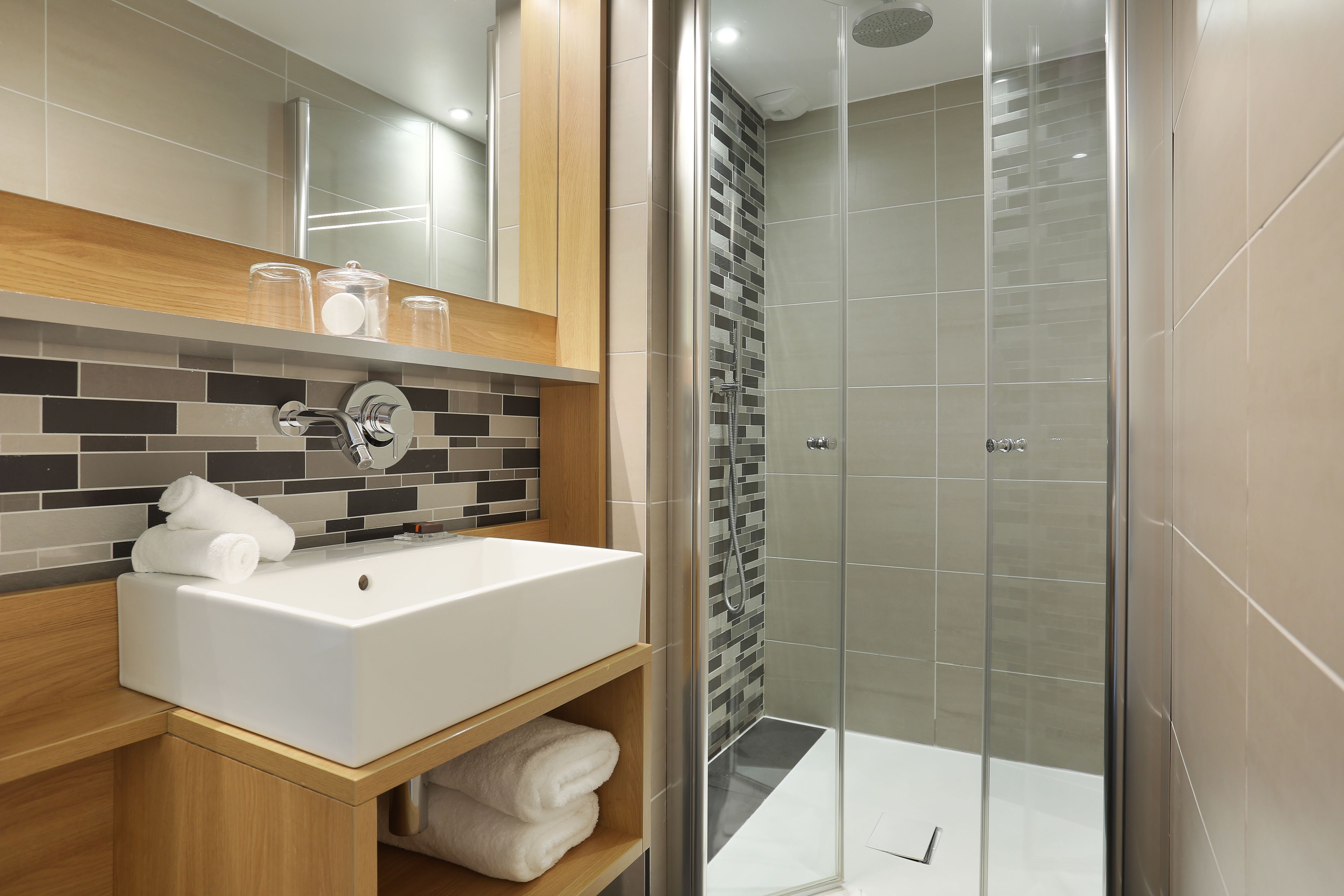 Un baño moderno con un lavamanos blanco, repisas de madera y una cabina de ducha de vidrio.