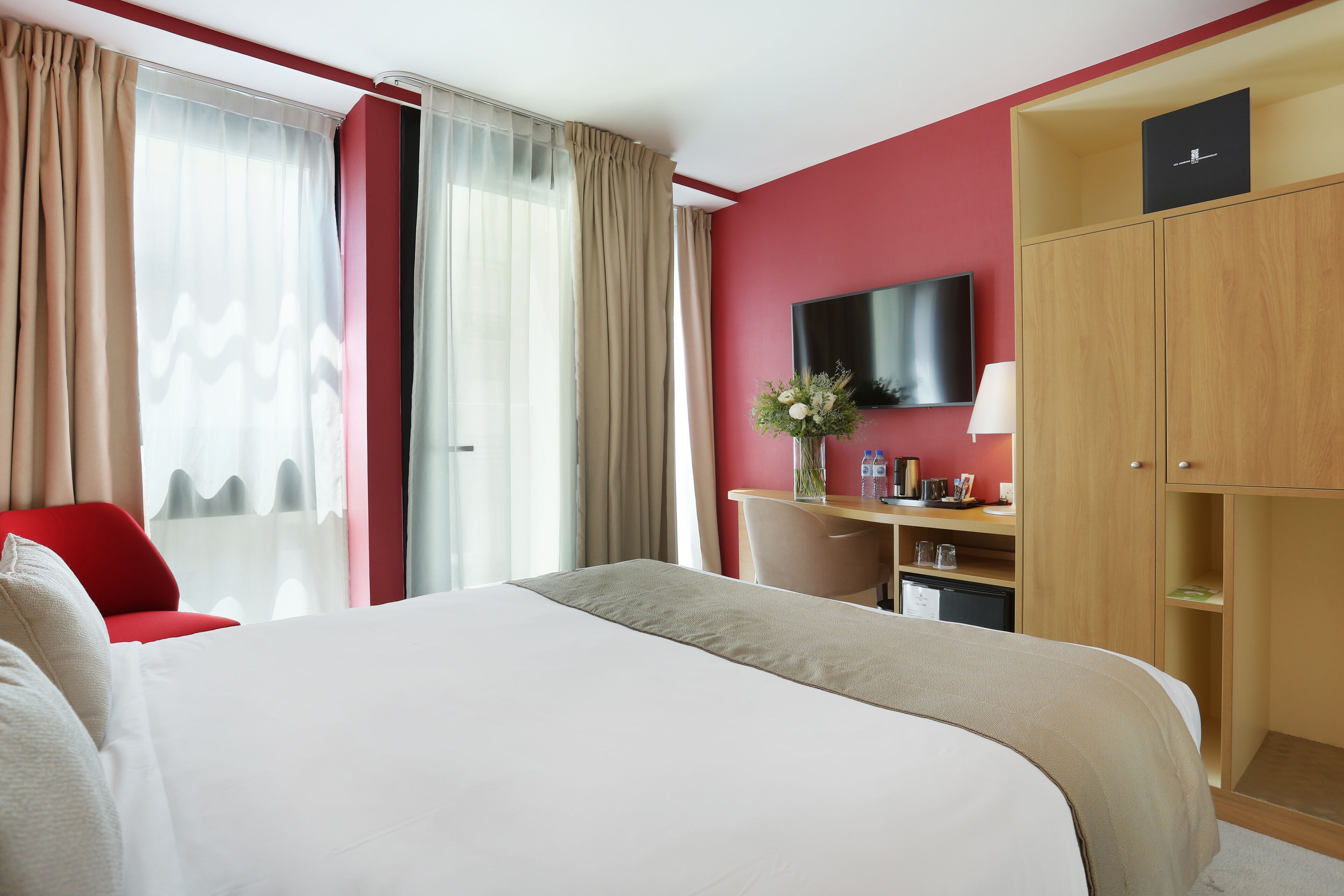A hotel room with a large bed, a desk, a TV, and a wardrobe.