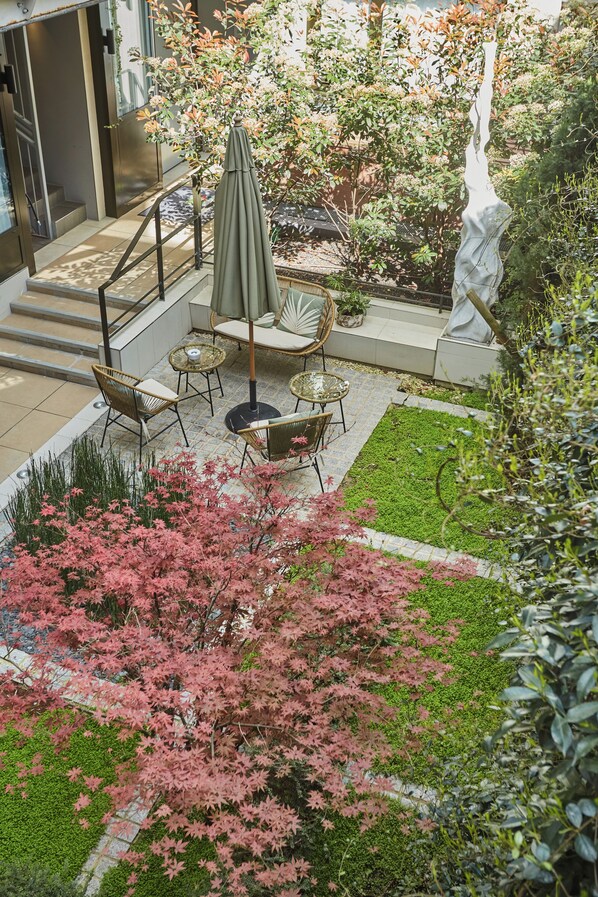 Un patio con mobiliario exterior, una estatua y un jardín con follaje rosado.