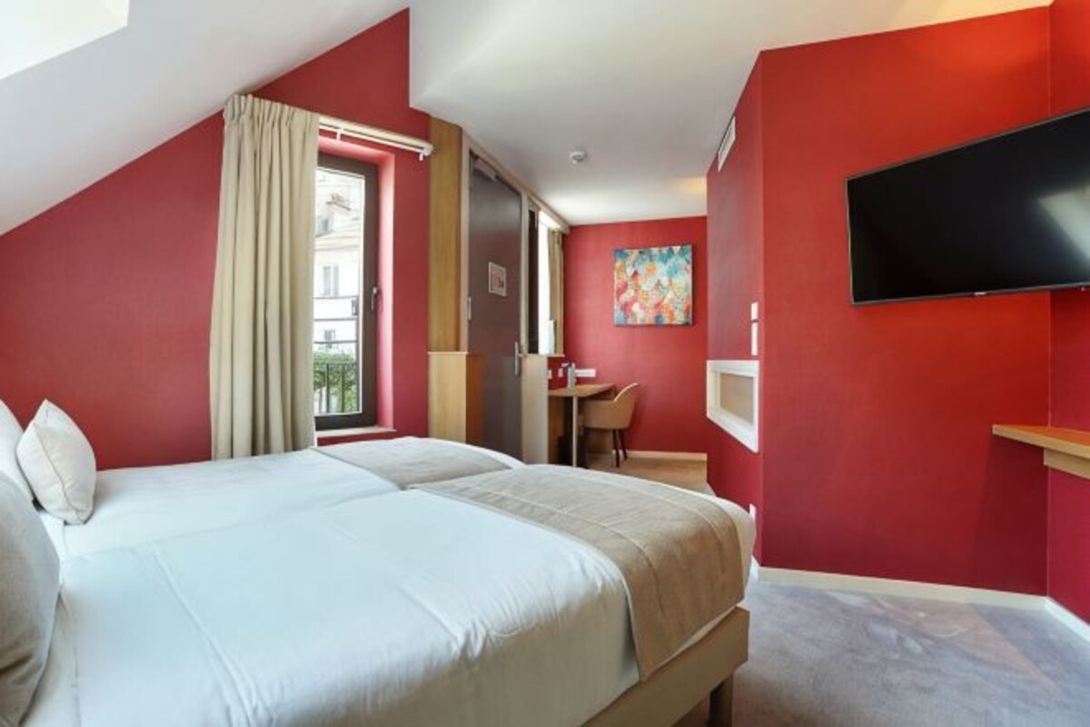 A hotel room with a bed, a desk, a chair, a TV, and a window with curtains.