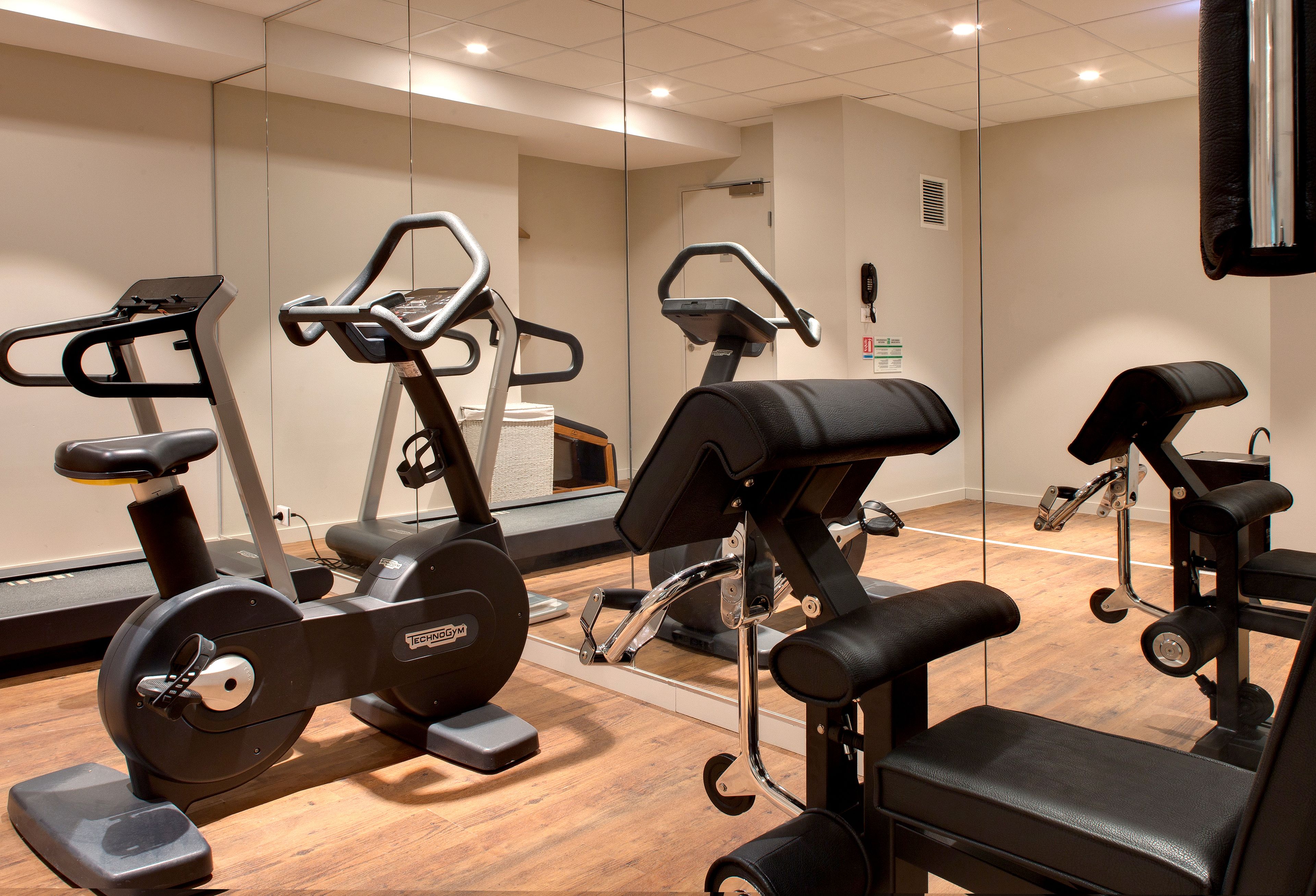 Ein Fitnessraum mit Trainingsgeräten, einem Spiegel und Holzboden.