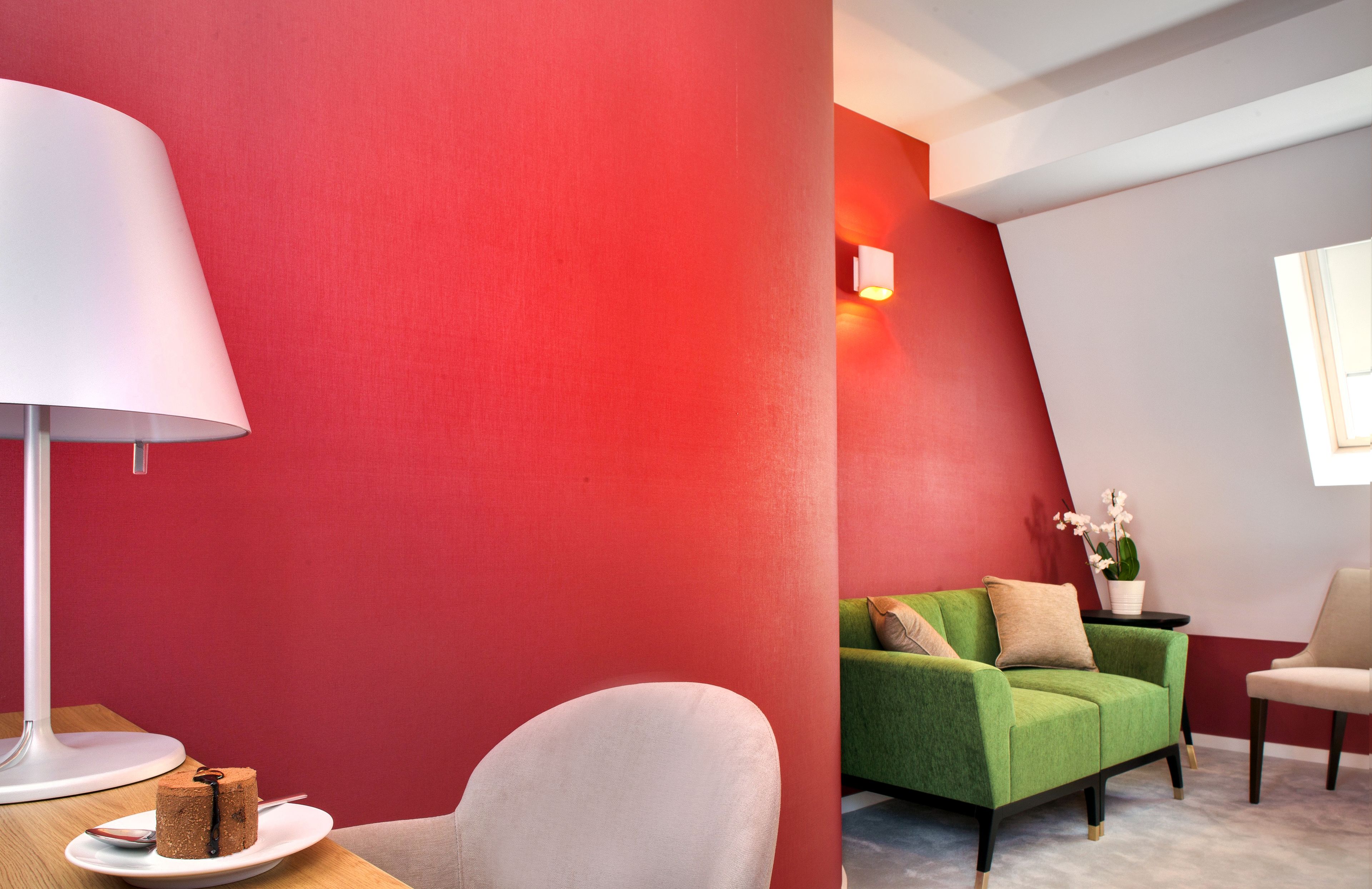 A modern room with a red accent wall, a green sofa, a white armchair, and a small table with a cake.
