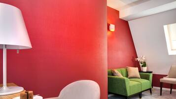 A modern room with a red accent wall, a green sofa, a white armchair, and a small table with a cake.
