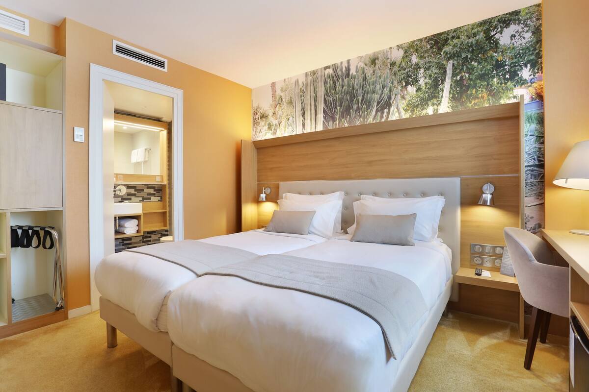 Ein Hotelzimmer mit einem großen Bett, einem Schreibtisch mit Stuhl, einem Spiegel und einem Wandbild.