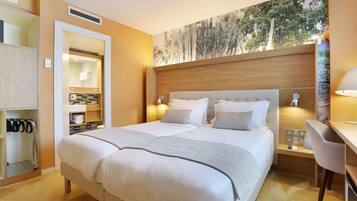 Habitación de hotel con una cama grande, un escritorio con silla, un espejo y una obra de arte colgada en la pared.