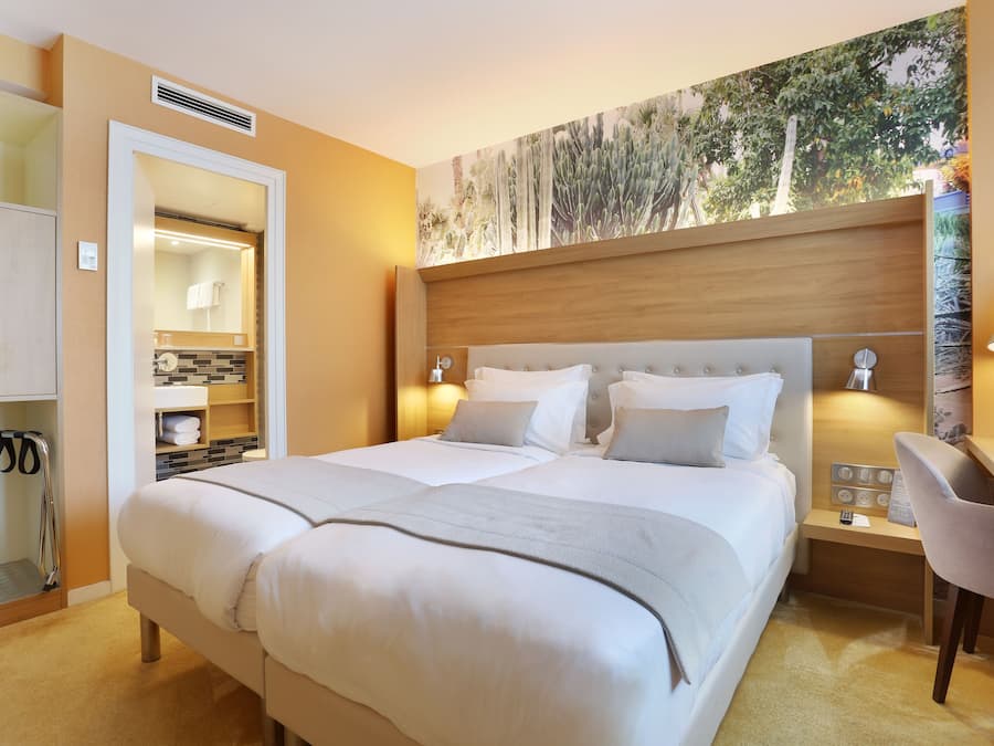 Habitación de hotel con una cama grande, un escritorio con silla, un espejo y una obra de arte colgada en la pared.