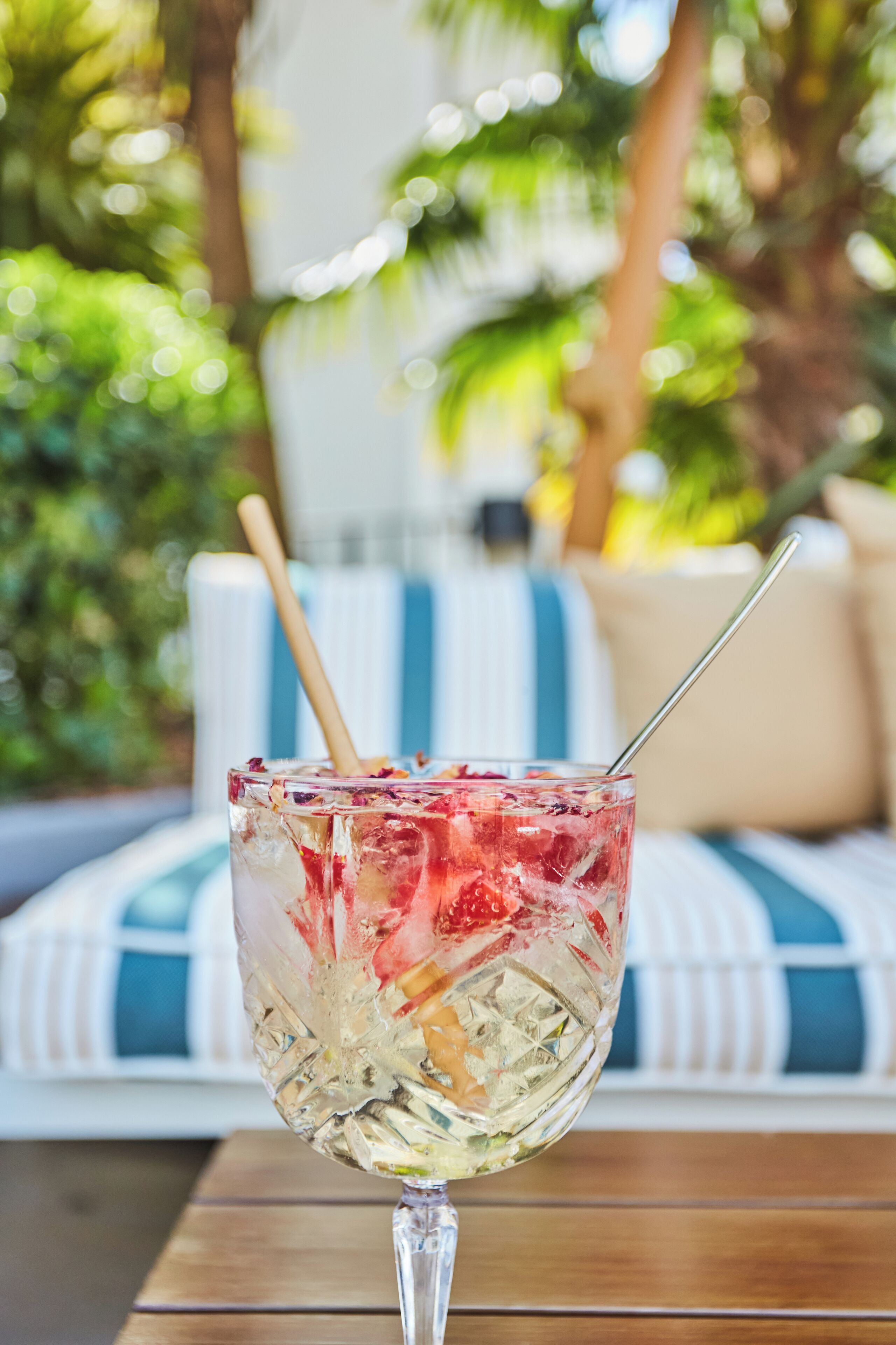 A glass with a straw on a wooden table with a white and blue striped cushion in the background.