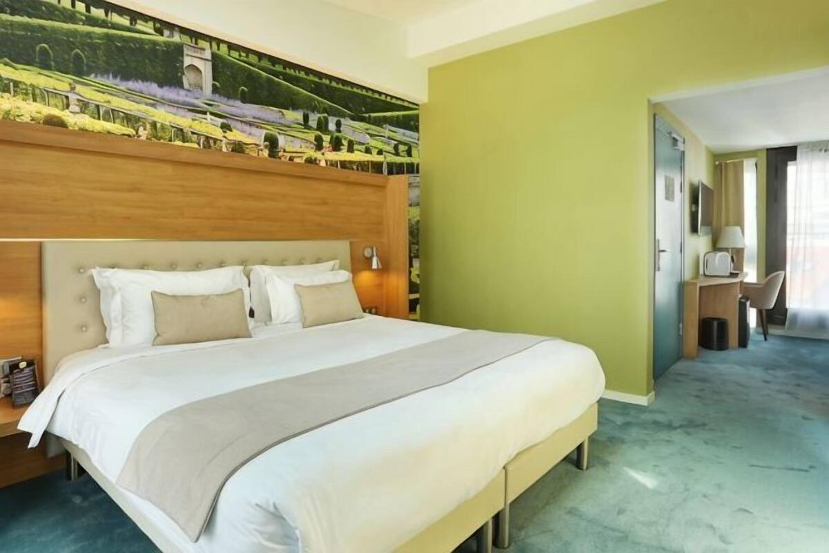 Ein Hotelzimmer mit einem großen Bett, einem Kopfteil, einem Schreibtisch mit Stuhl und Blick auf einen Garten.