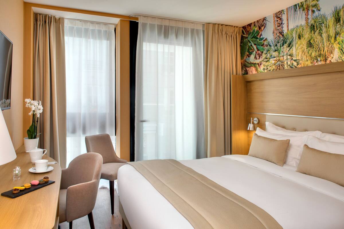 Ein Hotelzimmer mit Bett, Schreibtisch mit Stuhl, Fernseher und einem Fenster mit Vorhängen.