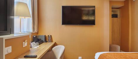 A hotel room with a desk, chair, bed, TV, and a window with curtains.