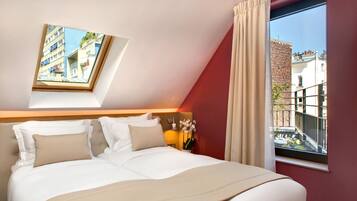 Une chambre d’hôtel avec un lit, une fenêtre avec des rideaux, une table de chevet avec une lampe et une vue sur les bâtiments à l’extérieur.