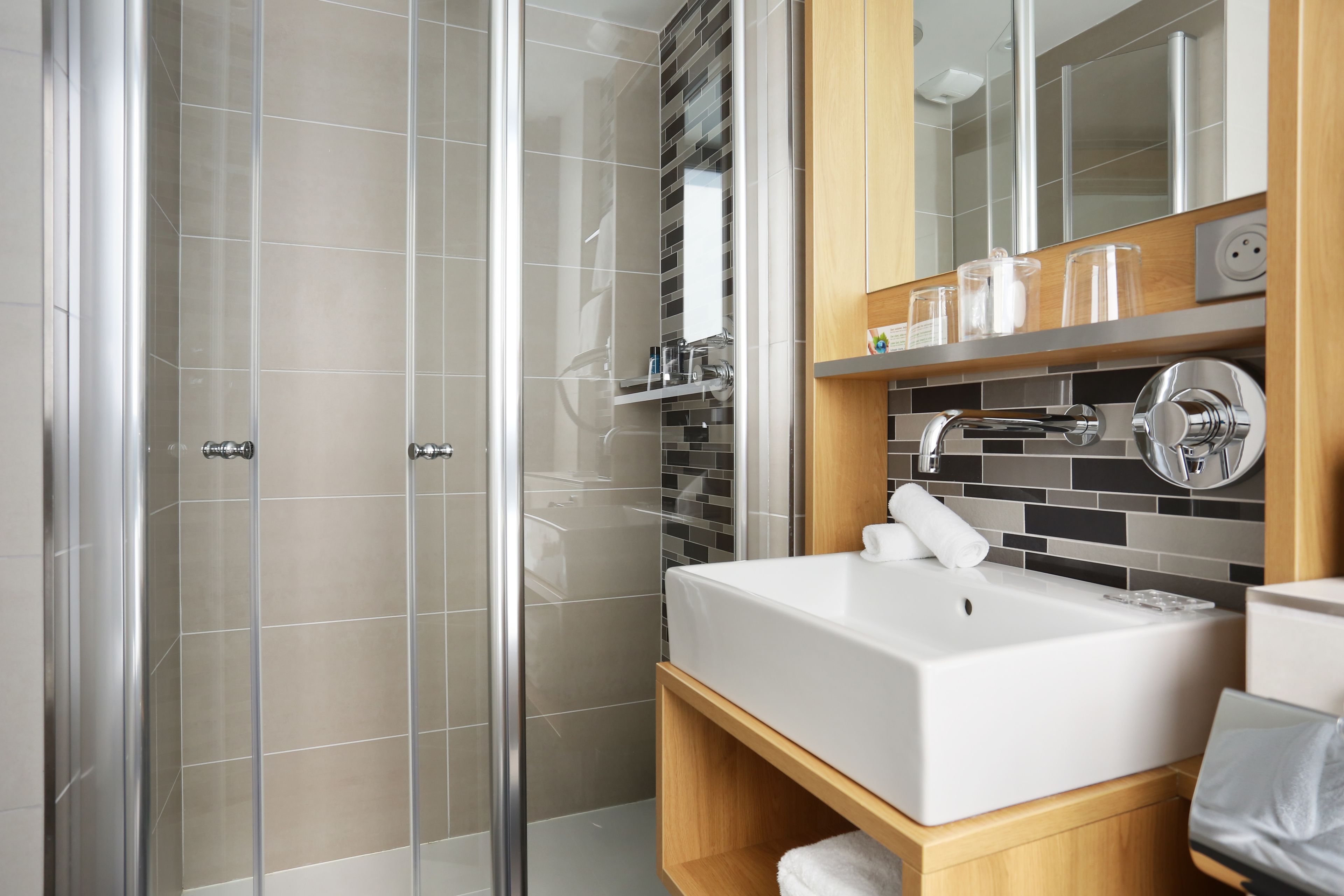 Un bagno moderno con doccia vetro, lavandino bianco e mobile bagno in legno.