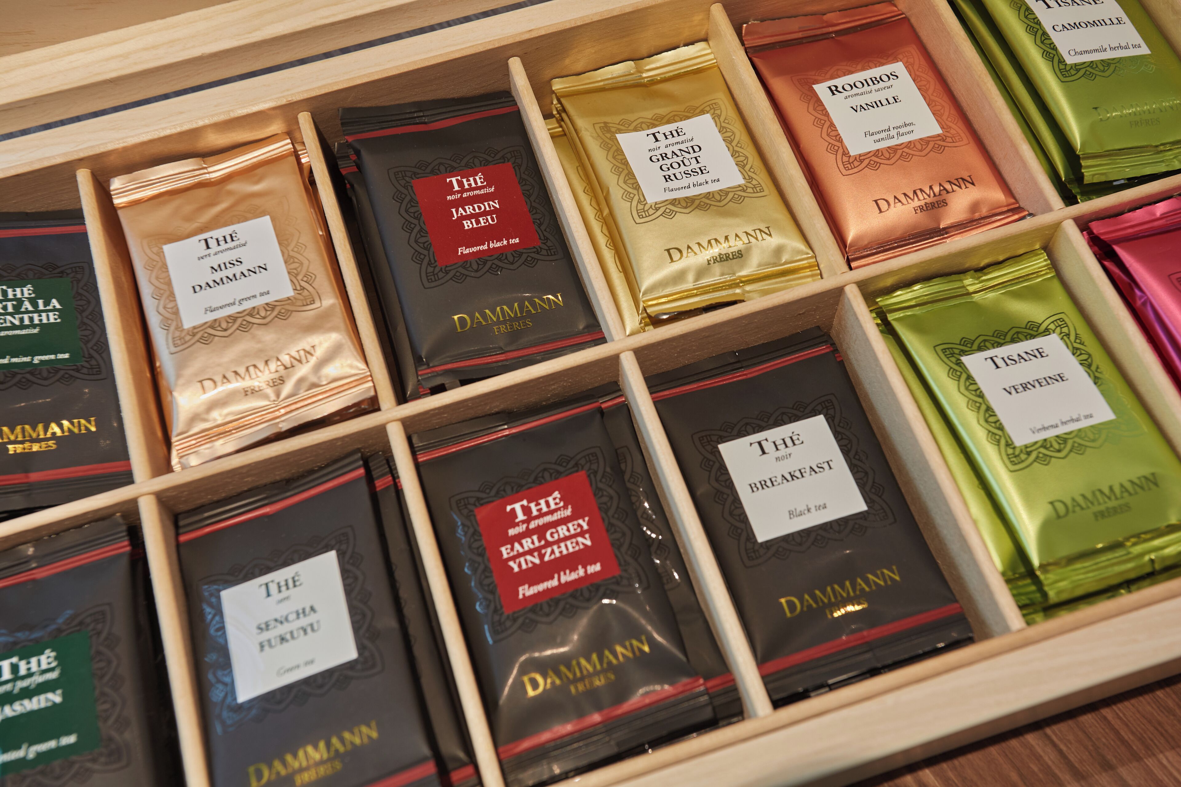 A wooden drawer with multiple compartments containing various tea boxes labeled with names and descriptions.