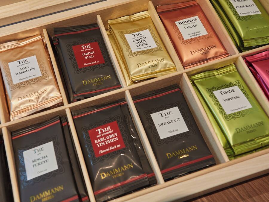 A wooden drawer with multiple compartments containing various tea boxes labeled with names and descriptions.