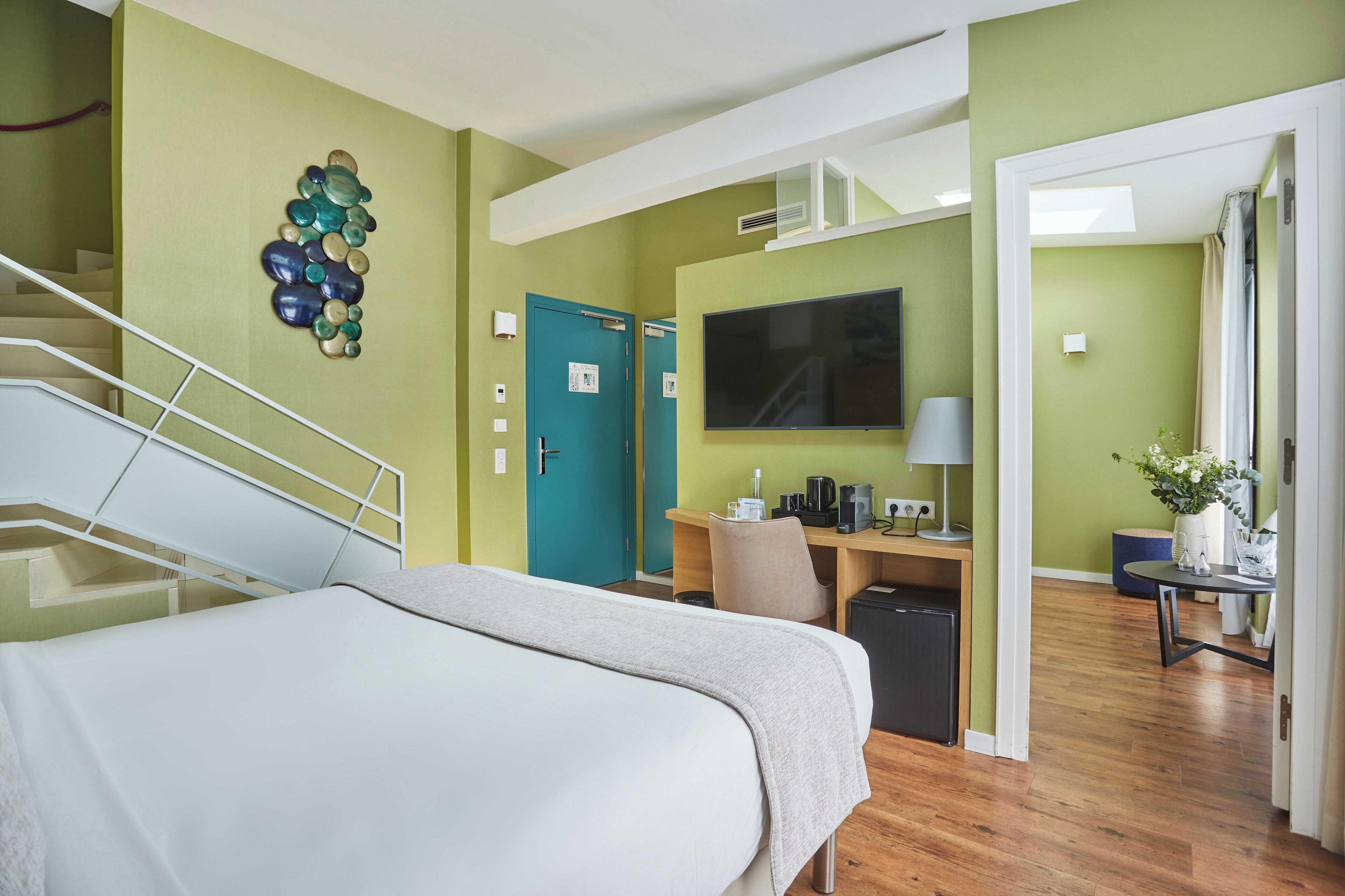 A hotel room with a bed, a desk with a computer, a TV, and a staircase.