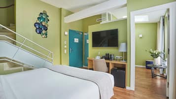 A hotel room with a bed, a desk with a computer, a TV, and a staircase.