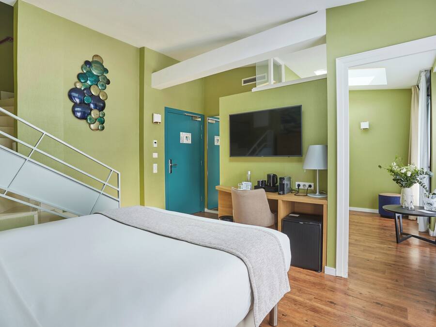 A hotel room with a bed, a desk with a computer, a TV, and a staircase.