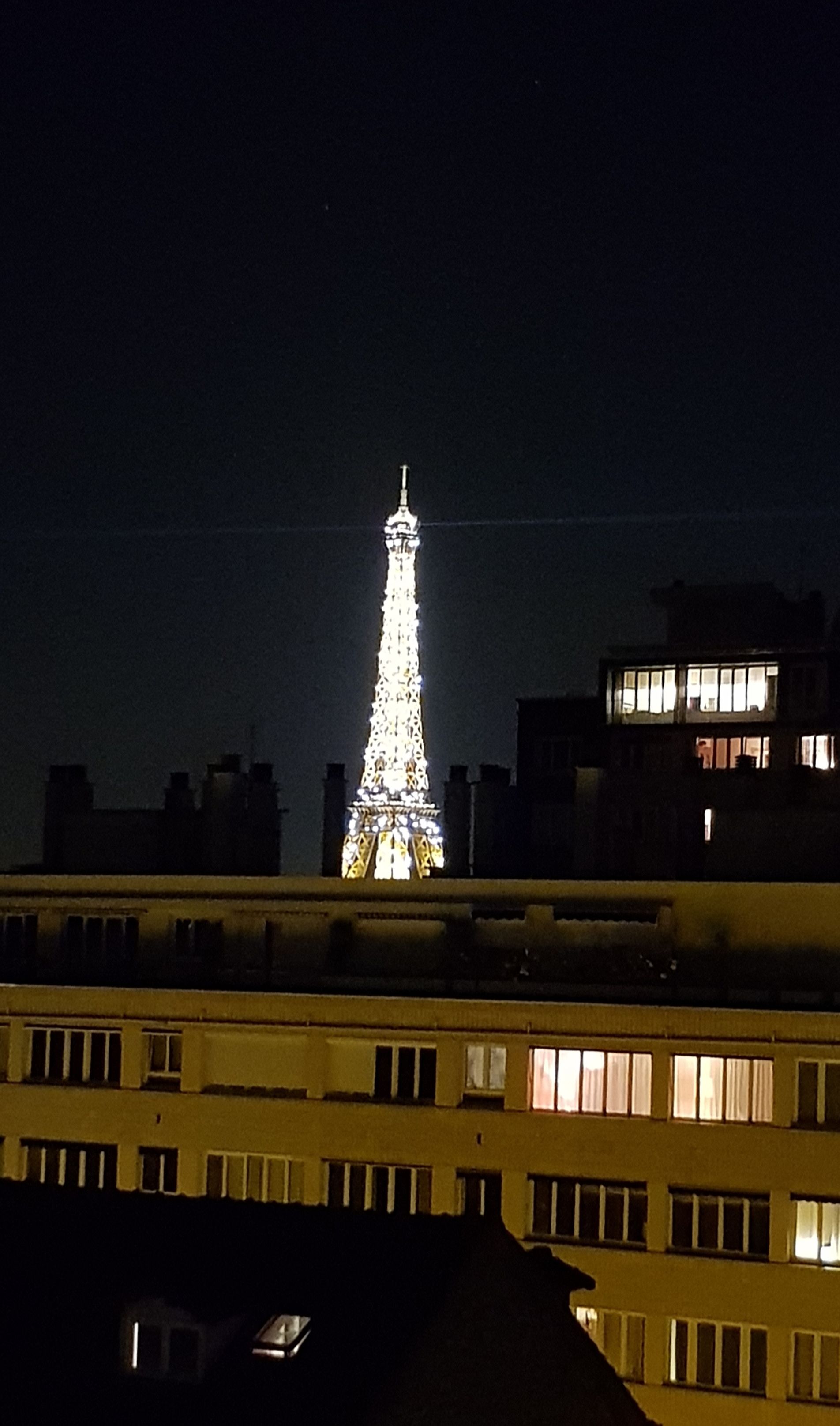 Ein Nachtblick auf den beleuchteten Eiffelturm vor dunklem Himmel, mit einem Gebäude im Vordergrund.