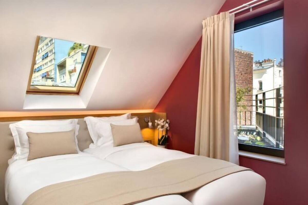 Ein Hotelzimmer mit Bett, einem Fenster mit Vorhängen, einem Oberlicht und Blick auf Gebäude.