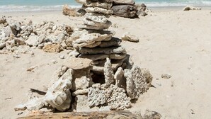 A stack of stones on a beach with a clear sky and mountains in the background. - maoMeno (Gili Meno)
