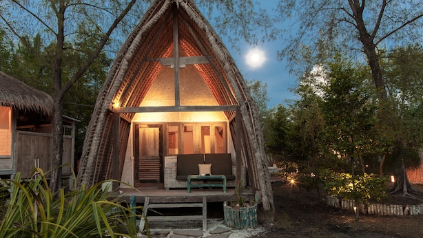 A thatched-roof hut with a wooden bench and cushions in front, surrounded by trees and a clear sky. - maoMeno (Gili Meno)