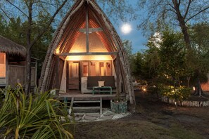 A thatched-roof hut with a wooden bench and cushions in front, surrounded by trees and a clear sky. - maoMeno (Gili Meno)