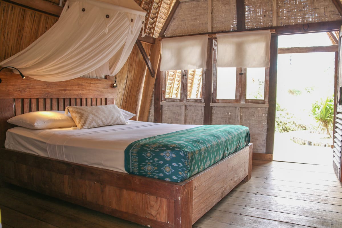 Una cama de madera con dosel, una colcha estampada verde y vistas al exterior a través de una ventana.