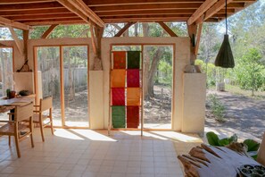 A covered patio with a dining area, large windows, and a view of the surrounding trees. - maoMeno (Gili Meno)