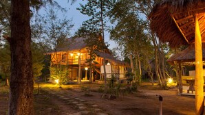 A rustic lodge with a thatched-roof structure, a large open patio, and a stone pathway leading to the entrance. - maoMeno (Gili Meno)