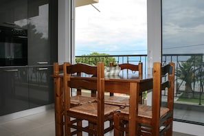 A dining area with a wooden table and chairs, large windows with a view of greenery and a cloudy sky.