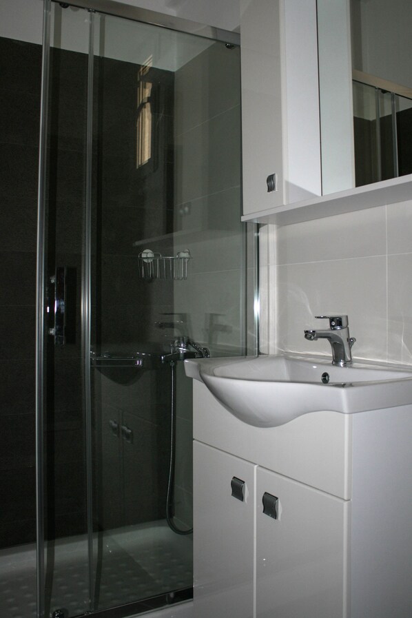 A modern bathroom with a glass shower enclosure, a white sink, and a cabinet. - Punda 4 Seasons (Aigialeia)