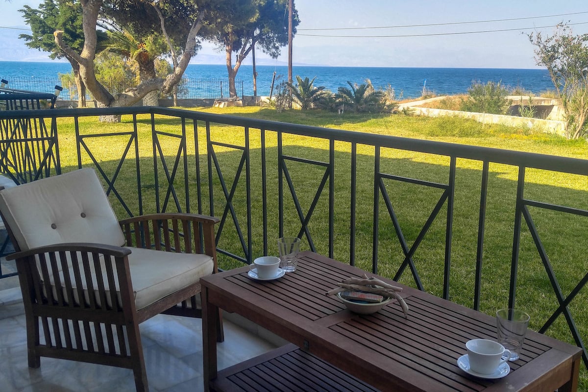 Un balcón con vista al mar, una mesa de madera y una silla acolchada.
