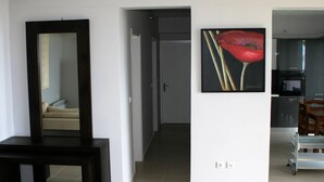Un pasillo con un espejo, un cuadro y una cocina visible a través de una puerta abierta.