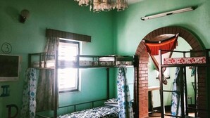 A room with bunk beds, a chandelier, a window with curtains, and a brick archway. - The Nepali Hive (Kathmandu)