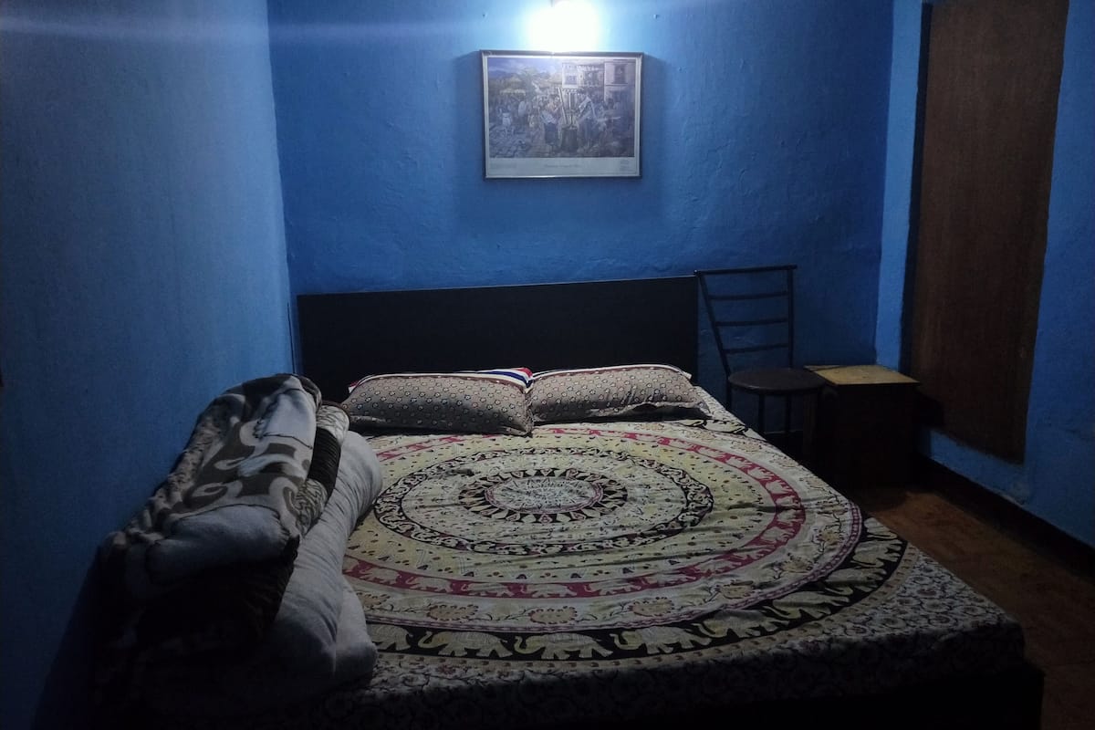A bedroom with a bed, pillows, a chair, a small table, and a wall-mounted picture.