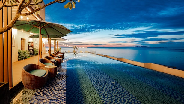 An infinity pool with a checkered floor, wicker chairs with cushions, and a view of the ocean at dusk. - HAIAN Beach Hotel & Spa (Da Nang)