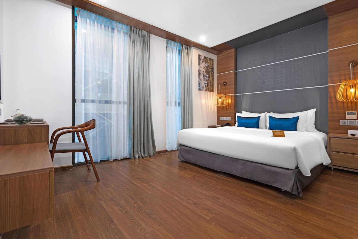 A modern hotel room with a large bed, wooden desk, and a chair.