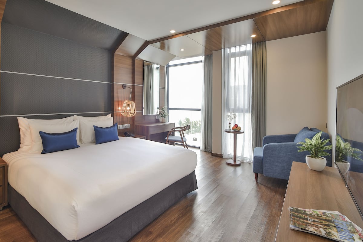 A modern hotel room with a large bed, a desk, a chair, and a balcony with a view.