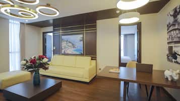 A modern hotel lobby with a yellow sofa, a coffee table with a vase of flowers, a wooden desk with a laptop, and a large painting on the wall.