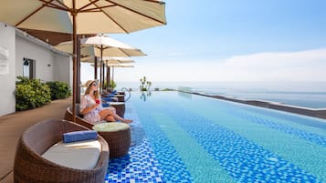 Zona de piscina con sillones de mimbre, sombrillas y vista al océano.