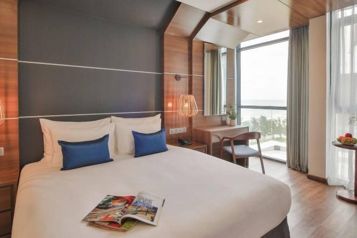A modern hotel room with a large bed, a desk, and a balcony with a view.