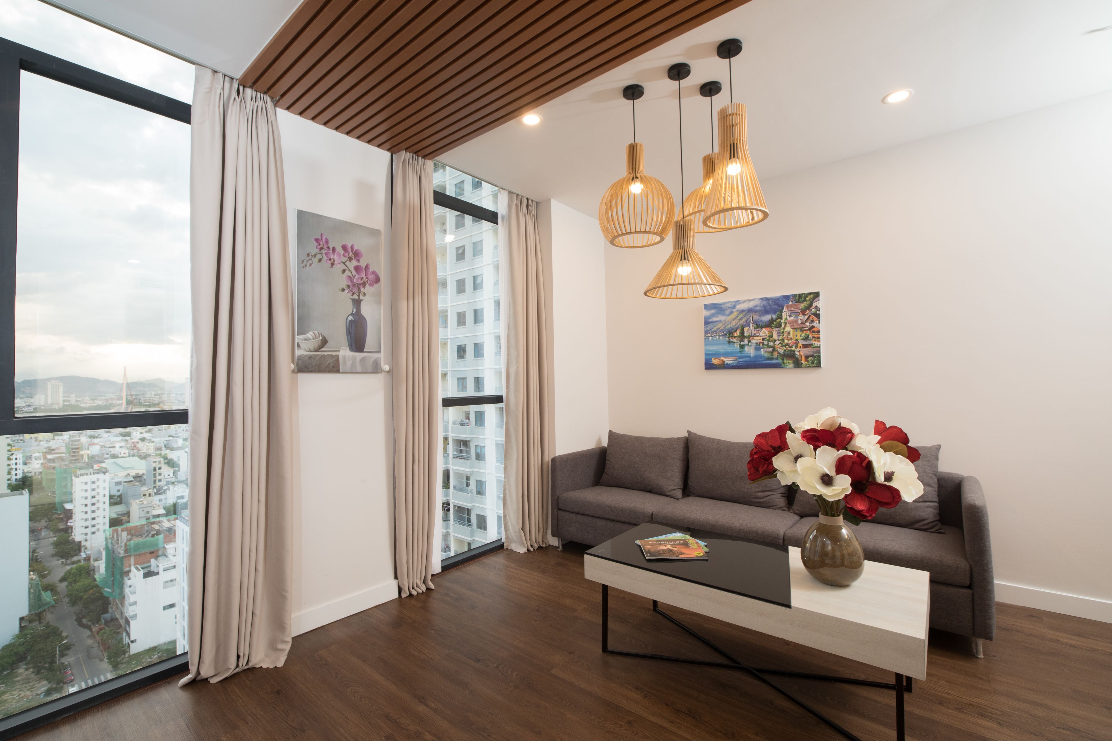 A modern living room with a large window, a grey sofa, a coffee table, and a vase of flowers.