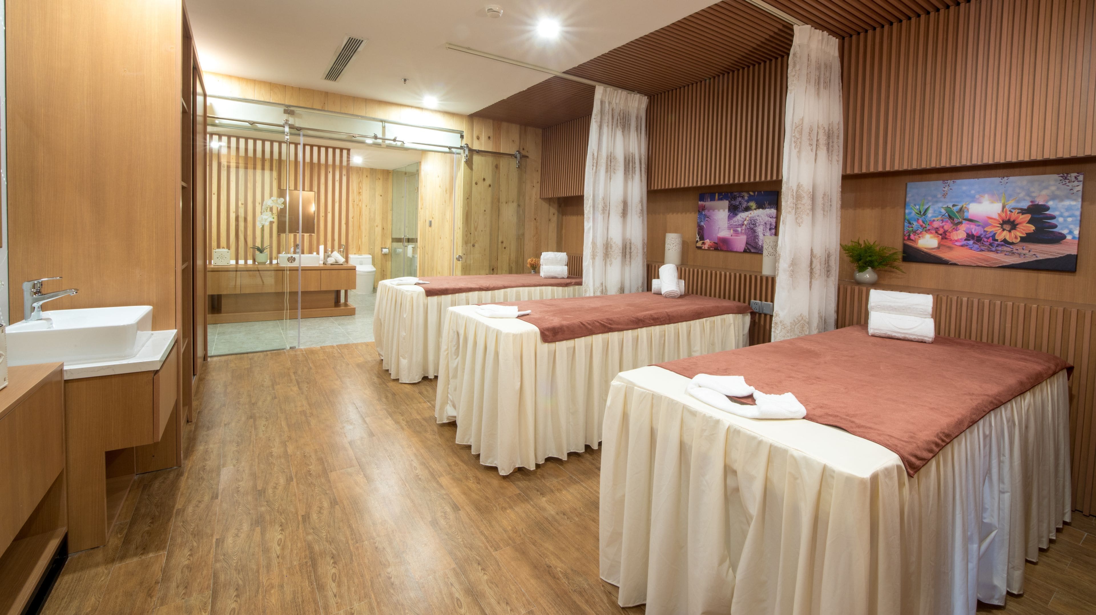 Een spa-ruimte met houten vloeren, een grote spiegel, een wastafel en drie massagetafels met handdoeken.