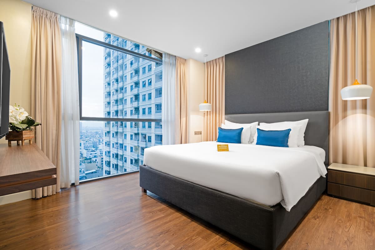 A modern hotel room with a large bed, a desk, and a view of a high-rise building.