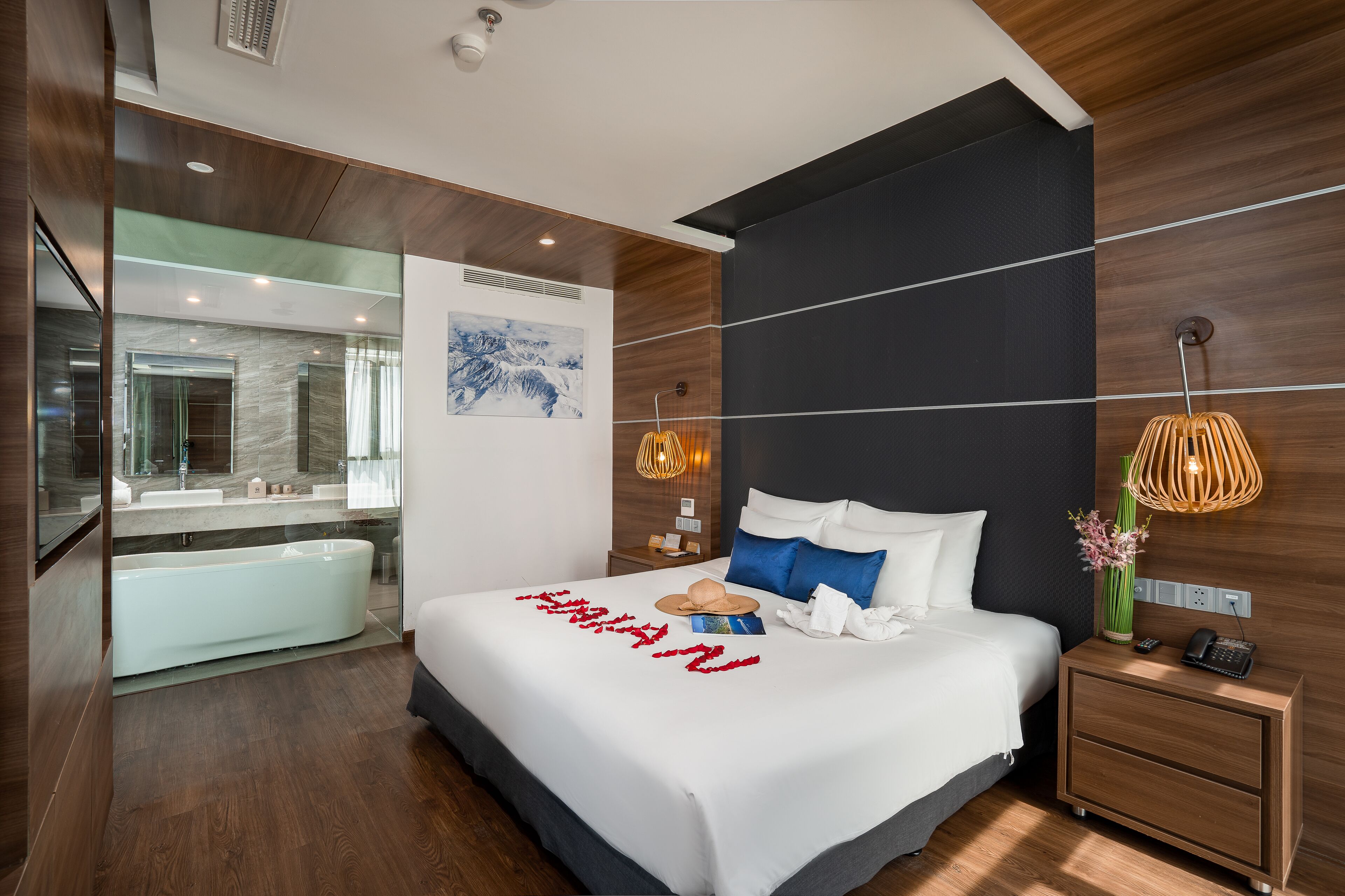 A modern hotel room with a large bed, a separate bathroom with a bathtub, and a view of the mountains.